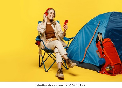 Full body young woman sit near bag stuff tent use mobile cell phone listening music in headphpnes isolated on plain yellow background. Tourist walk on spare time. Hiking trek rest travel trip concept - Powered by Shutterstock