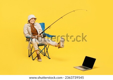 Full body young woman sit near laptop pc computer hold fishing rod pov pull isolated on plain yellow background. Tourist lead active lifestyle walk on spare time Hiking trek rest travel trip concept