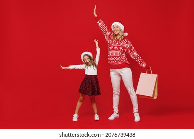 Full Body Young Woman In Sweater Hat With Child Baby Girl 6-7 Years Old. Mommy Little Kid Daughter Hold Shopping Package Bags With Purchases Isolated On Plain Red Background. New Year Family Concept