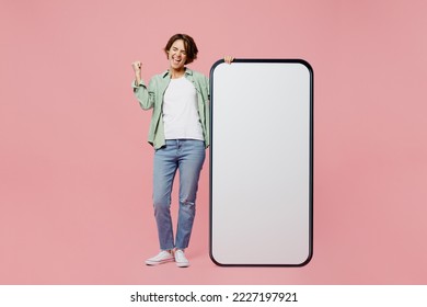 Full body young woman wear green shirt white t-shirt near big huge blank screen mobile cell phone smartphone with workspace mockup area do winner gesture isolated on plain pastel light pink background - Shutterstock ID 2227197921