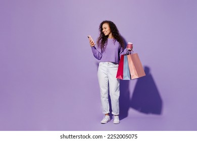 Full body young woman wear pullover hold in hand paper package bags after shopping cup coffee use mobile cell phone isolated on plain pastel light purple background. Black Friday sale buy day concept - Powered by Shutterstock