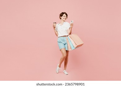 Full body young woman wear casual clothes hold shopping package bags takeaway delivery cup coffee to go use mobile cell phone isolated on plain pink color background. Black Friday sale buy day concept