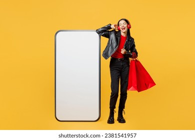 Full body young woman wear casual clothes red hat hold shopping package bags big huge blank screen mobile cell phone listen music isolated on plain yellow background. Black Friday sale buy day concept - Powered by Shutterstock