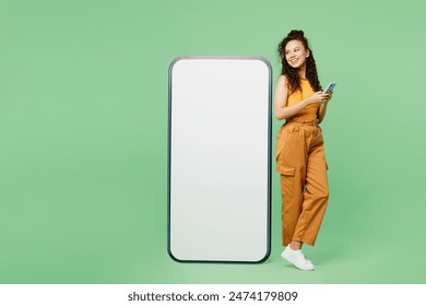 Full body young woman wear yellow tank shirt top big huge blank screen mobile cell phone with workspace copy space mockup area using smartphone isolated on plain green background. Lifestyle concept