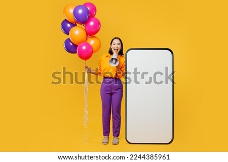 Full body young woman wear casual clothes hat celebrating near big huge blank screen area mobile cell phone scream in megaphone isolated on plain yellow background. Birthday 8 14 holiday party concept