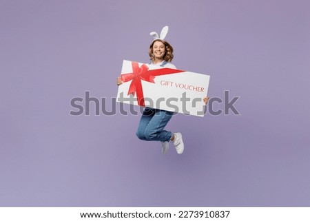 Full body young woman wear casual clothes bunny rabbit ears hold store big gift certificate coupon voucher card isolated on plain pastel light purple background studio. Lifestyle Happy Easter concept