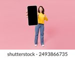 Full body young woman wearing yellow sweatshirt casual clothes hold in hand use blank screen mobile cell phone show thumb up isolated on plain pastel light pink background studio. Lifestyle concept