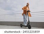 Full body young woman wears orange shirt casual clothes riding e-scooter transport listen music in headphones walking rest relax in spring green city park outdoors on nature. Urban lifestyle concept