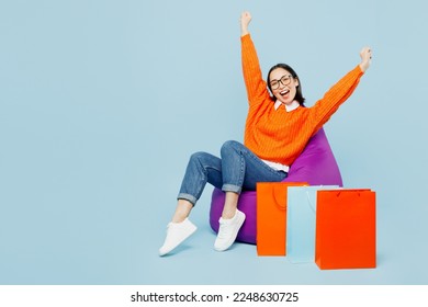 Full body young woman wears orange sweater sit in bag chair near paper package bags after shopping isolated on plain light pastel blue cyan color background studio. Black Friday sale buy day concept - Powered by Shutterstock