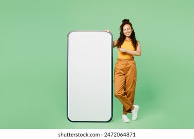 Full body young woman wears yellow tank shirt top point index finger on big huge blank screen mobile cell phone smartphone with copy space area isolated on plain green background. Lifestyle concept - Powered by Shutterstock