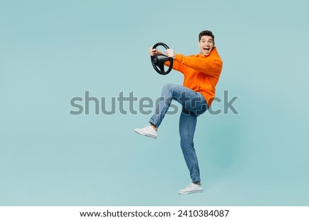 Full bodyside view young man wears orange hoody casual clothes hold steering wheel driving car raise up leg isolated on plain pastel light blue cyan color background studio portrait. Lifestyle concept