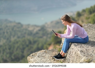Full bofy side view portrait of a happy teen checking smart phone in a cliff