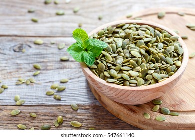 Full bowl of pumpkin seeds close up on a wooden table.