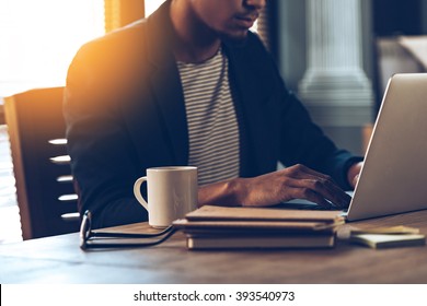 Full concentration. Close-up part of young African man using laptop while sitting at his working place - Powered by Shutterstock