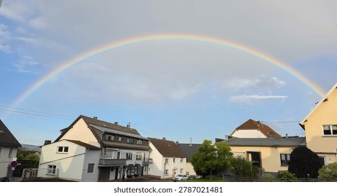 Full double rainbow arching over residential neighborhood with traditional German houses in Dorndorf, Hessen, Germany after summer rain