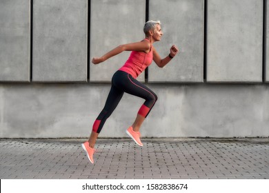 Full of energy. Side view of active middle aged woman in sport clothing jumping while exercising outdoors. Healthy lifestyle concept. Sport after 50