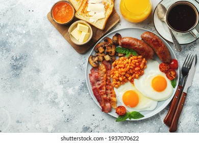 Full English breakfast on a plate with fried eggs, sausages, bacon, beans, toasts and coffee on light stone background. With copy space. Top view.