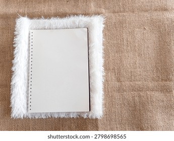 Full flat lay view of a small blank white spiral planner surrounded by a cozy soft fur layer on textured sackcloth.