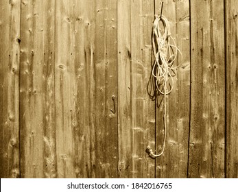 Full format view of a weathered board wall of a cattle shed with a rope attached to a nail; toned in Sephia.