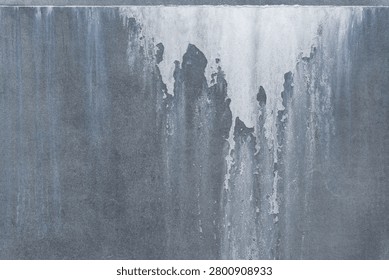 Full frame abstract background of a weathered grey cement tile panel with severe water damage and white salt stains. Rough industrial concrete surface with mineral efflorescence deposits, moisture defects and chemical erosion.