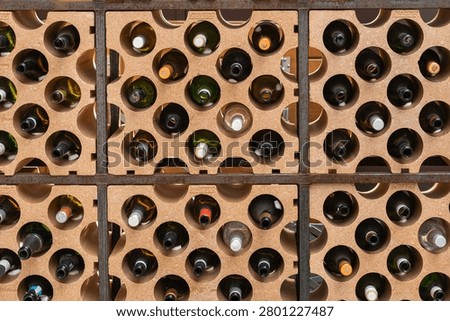 Full frame background of multiple wine bottles stored horizontally in a modular clay honeycomb rack inside a cellar.