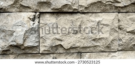 Full frame background of a rustic natural stone wall with rectangular blocks. The stones feature a rough, chiseled texture and earthy beige tones, ideal for architectural or construction-themed backgrounds.