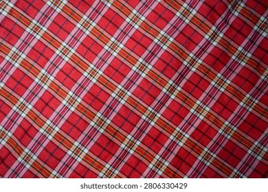 Full frame background texture of a red plaid tartan fabric with criss-crossed lines pattern.