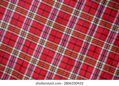 Full frame background texture of a red plaid tartan fabric with criss-crossed lines pattern.