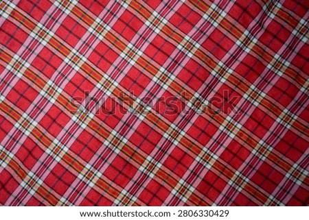 Full frame background texture of a red plaid tartan fabric with criss-crossed lines pattern.