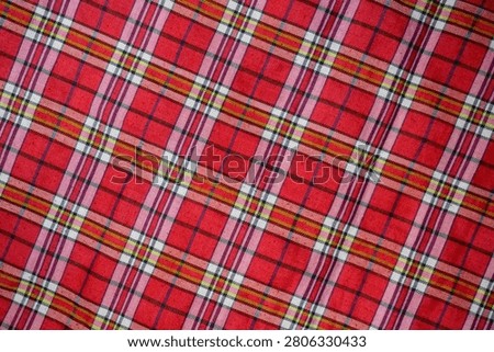 Full frame background texture of a red plaid tartan fabric with criss-crossed lines pattern.