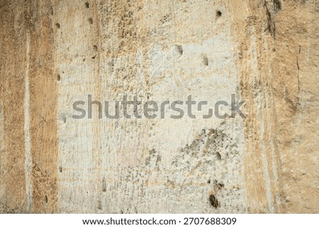 Full frame background texture of a rough, weathered sand-colored quarry wall with small holes and vertical line erosion marks