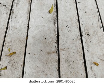 Full frame background texture of weathered white painted wooden planks with scattered tiny dry leaves. Close-up top view of a rustic weathered white wooden deck surface with a few small fallen leaves during daytime.