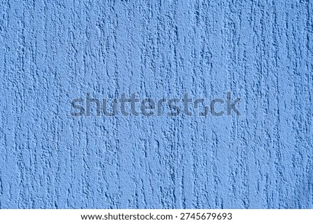Full frame close up of a bright blue exterior wall with a rough decorative plaster texture under direct sunlight