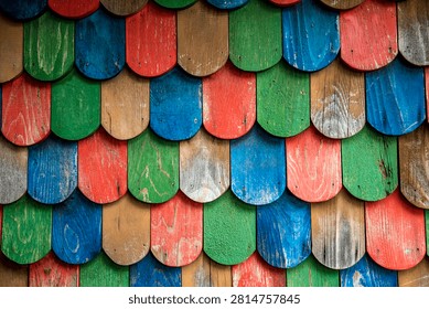 Full frame close-up background texture of rustic, rounded wooden shingles or roof shakes painted in alternating bright colors including blue, red, green, and natural wood tones.