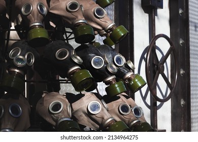 A full frame dark image of rows of gas masks with bright green filters on them and blue glass eyepieces. Bunker with round valve is on the side of the frame. Dark scary war picture