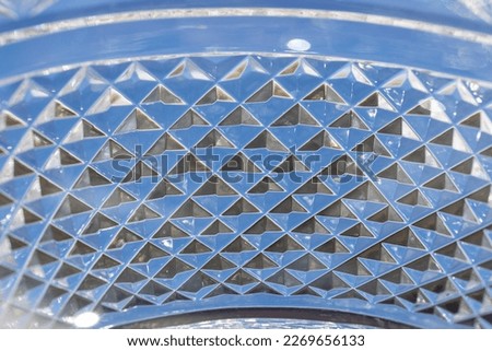 Full frame defocused macro abstract of a lead crystal glass bowl surface with diamond facet cuts and blue sky background