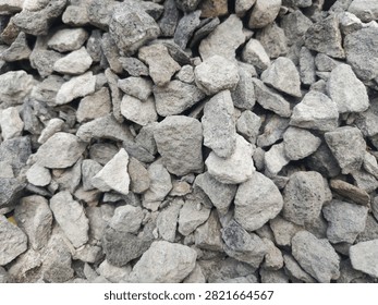 Full frame high-angle shot of raw crushed gray stones and sub-angular gravel pieces. This detailed industrial texture highlights the natural sharp edges, variations in shades, and rugged surfaces of building aggregates. It is an ideal background material for concepts related to civil engineering, road paving infrastructure, concrete mixture manufacturing, and architectural foundations