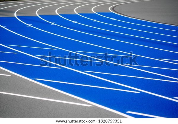 Full frame\
image in natural light of textured curved surface of a clean, new\
outdoor blue running track with white lines, gray border and copy\
space. Selective focus on\
foreground.