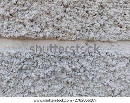 Full frame macro texture of a white roughcast stucco concrete wall featuring a smooth horizontal groove dividing the rough plaster surface.