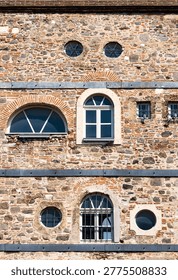 Full frame texture of an ancient stone and red brick wall featuring various architectural window styles including arched circular and square shapes.