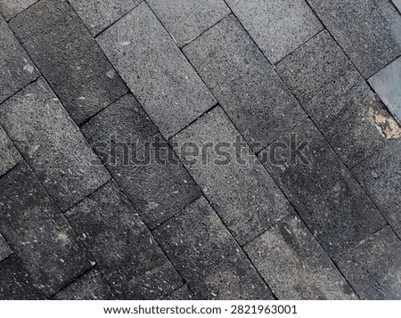 Full frame view of a dark grey volcanic stone block wall texture. The rectangular natural stone tiles feature a coarse, grainy surface and running bond pattern, suitable for modern architectural backgrounds.