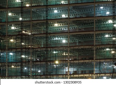 a full frame view of a large construction site at night illuminated by bright work lights with girders and construction hoists