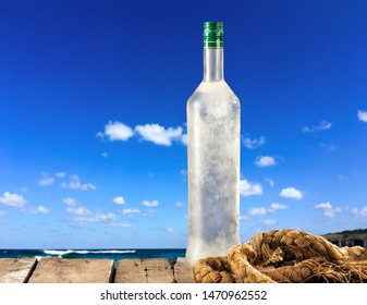 Full Frozen Ouzo Bottle On Wooden Table On Sky Background