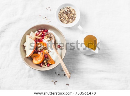 Full fruit and greek yogurt breakfast bowl. Persimmon, apple, walnuts, pomegranates and natural yogurt. Healthy food concept on light background, top view     