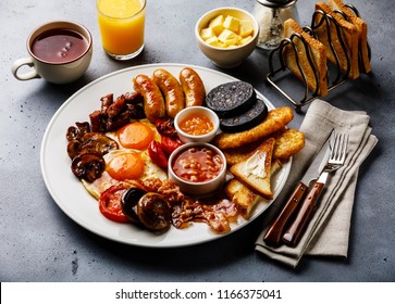 Full fry up English breakfast with fried eggs, sausages, bacon, black pudding, beans, toasts and tea on gray concrete background