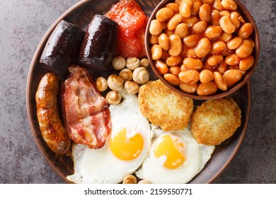 Full Fry Up English Breakfast With Fried Eggs, Sausages, Bacon, Black Pudding, Beans, Tomato Closeup In The Plate On The Table. Horizontal Top View From Above
