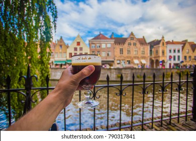 Full glass of beer on Brugge cityscape background. Hand with beer glass in Bruges, Belgium.