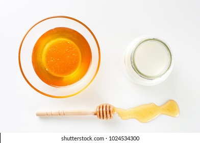 Full glass bowl and wooden stick dipper with pool of honey on white background