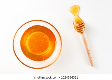 Full glass bowl and wooden stick dipper with pool of honey on white background