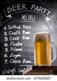 Full Glass Of The Cold Beer With Foam On A Wooden Table At Background Of A Chalk Board With Menu Text, Bottom-up View. Draft Beer On A Bar Counter In A Pub.